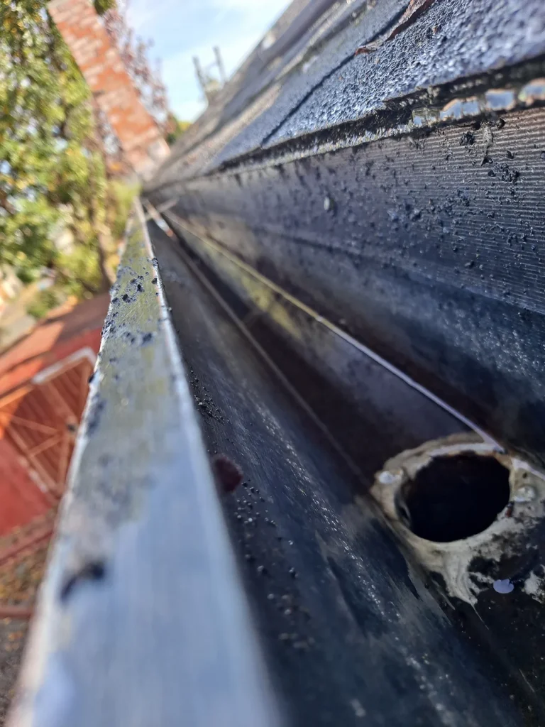 Looking along a roof gutter filled with grit and standing water beside the outlet