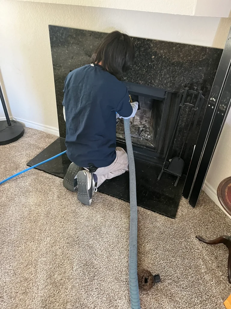 A technician vacuuming inside a black fireplace insert on a carpeted floor