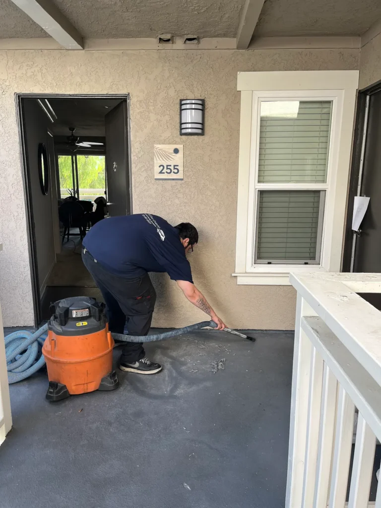 A technician vacuuming a covered entry walkway with a shop vacuum