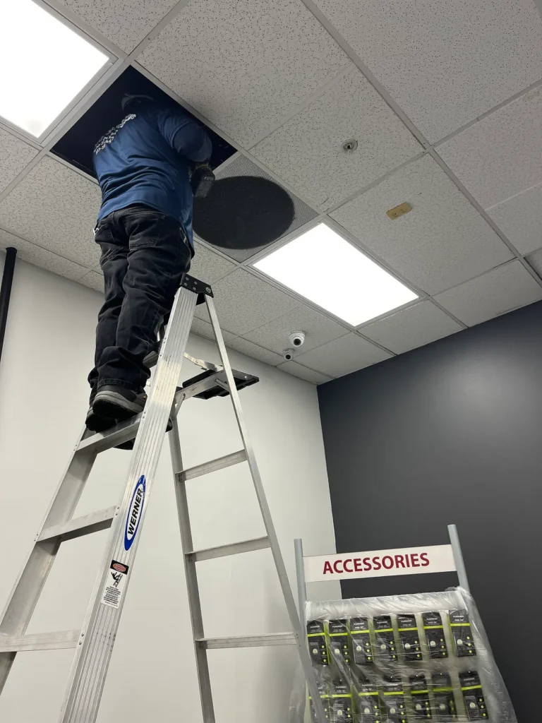 A technician up a ladder through an open ceiling tile in a commercial store