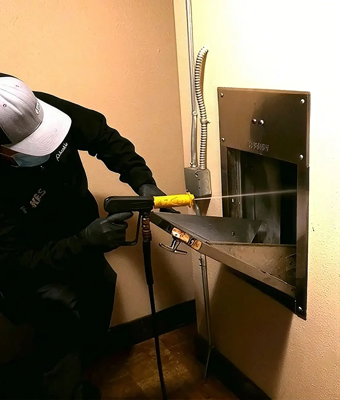 A worker cleaning inside a trash chute access door in a building hallway