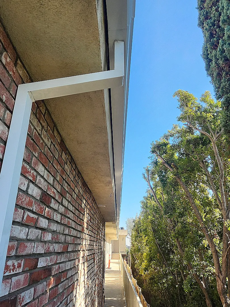 A clean white gutter running the length of the brick wall after the work