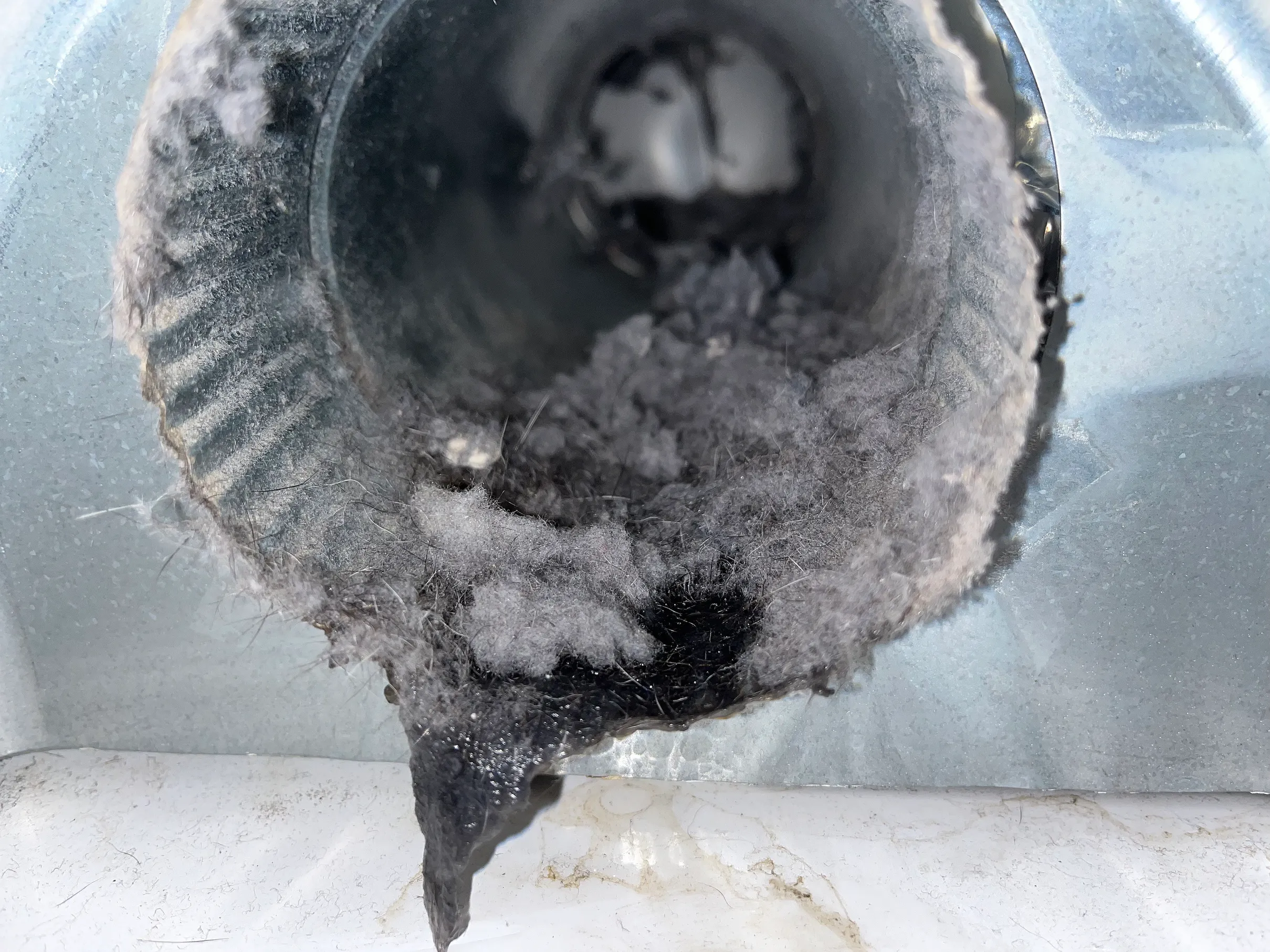 A dryer duct opening packed solid with gray lint before cleaning