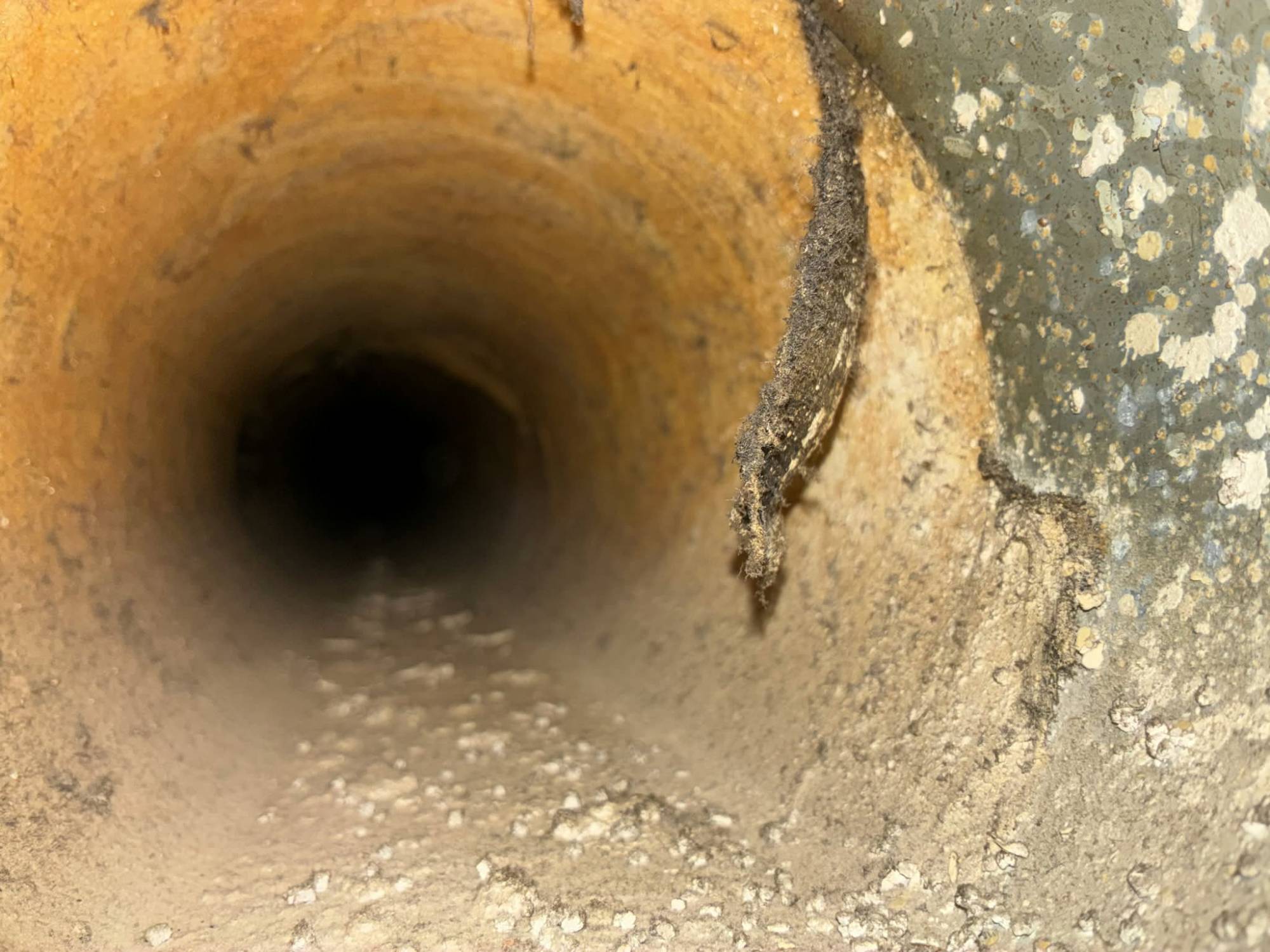 Inside a round duct where the fiberglass lining has broken down, with a strip of loose fiber hanging away from the duct wall