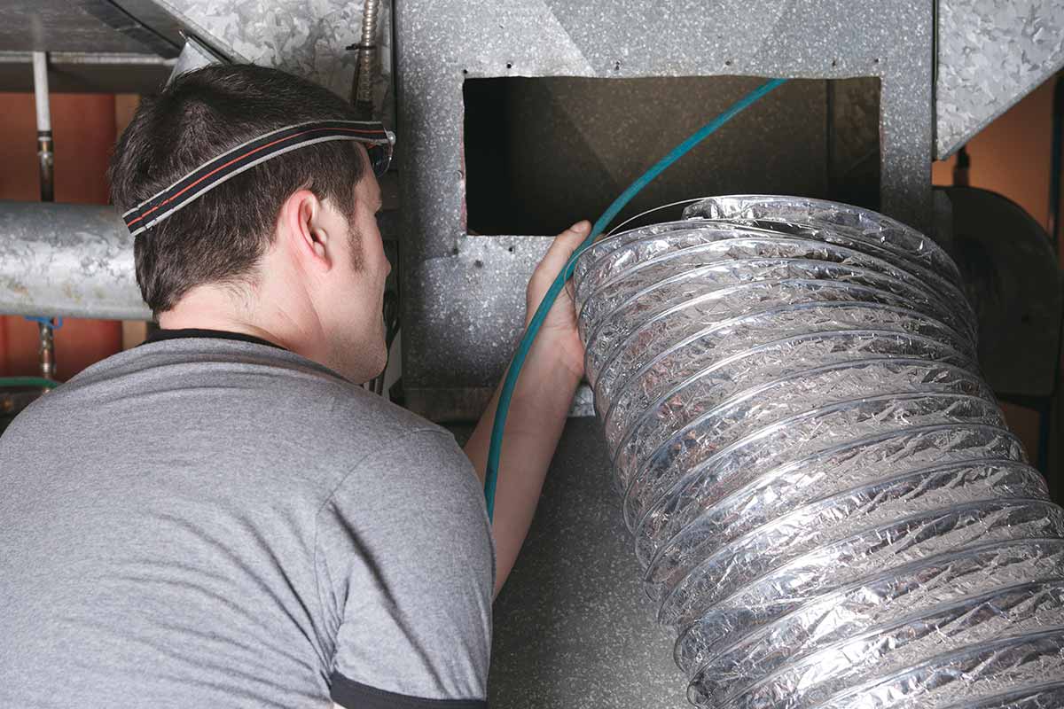 A technician feeding flexible ducting into an opening in commercial ceiling plant