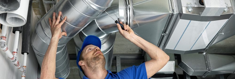 A technician in a blue cap reaching up to joint metal ducting