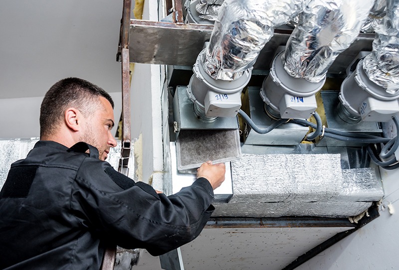 A technician working on insulated ductwork in a mechanical room