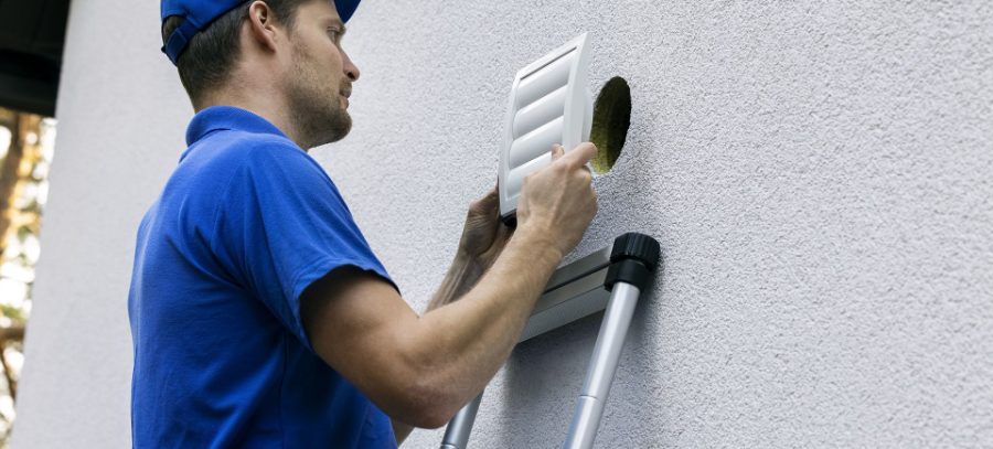 A technician fitting a louvered cover onto an exterior wall vent